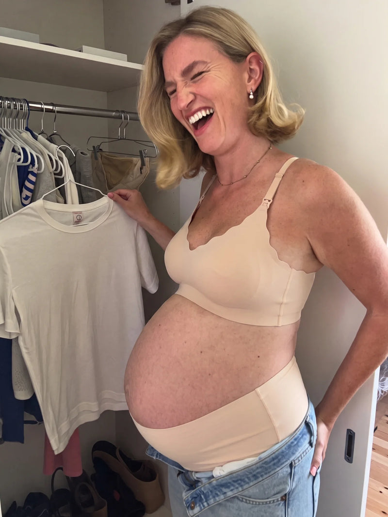 Pregnant mom laughing while picking a top in the Aura Comfort Bra in Skin