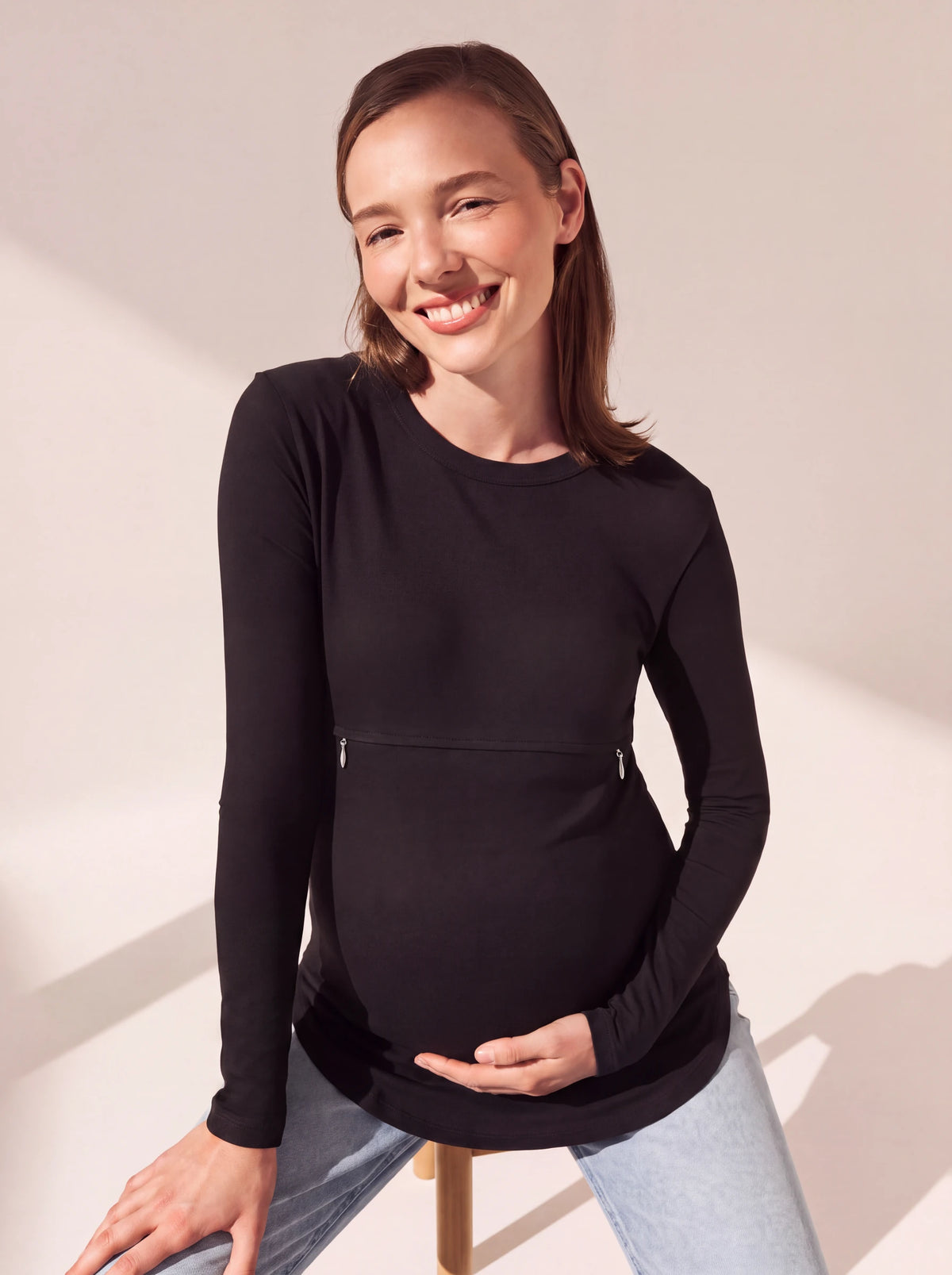 Pregnant woman seated on a stool in the black nursing tee