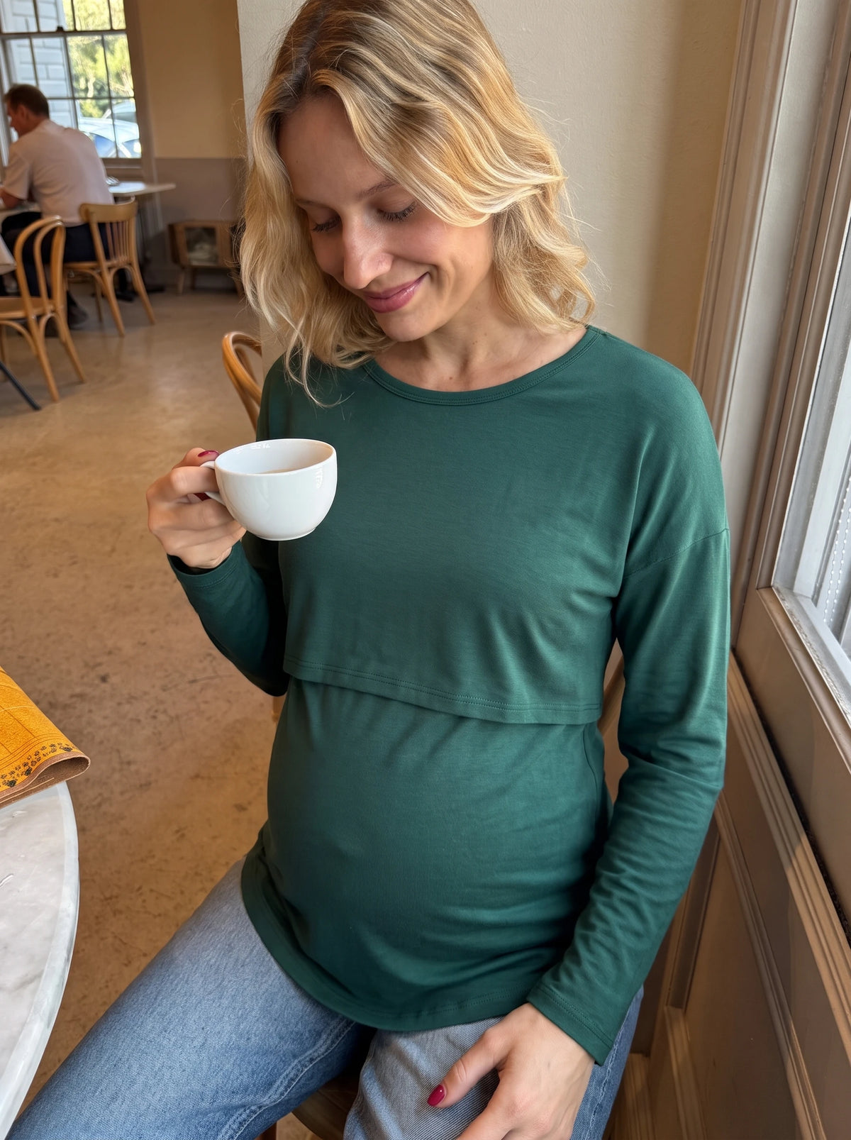 Pregnant woman in a cafe wearing the forest green layered nursing top