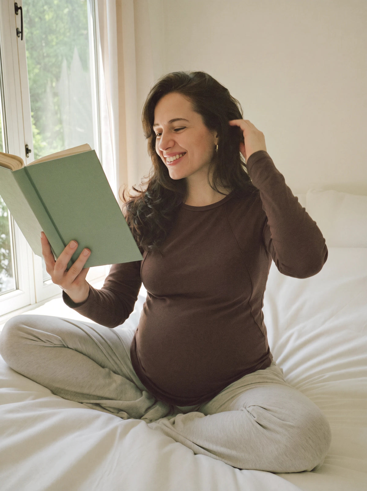 Mom reading on the bed in brown long sleeve nursing tee