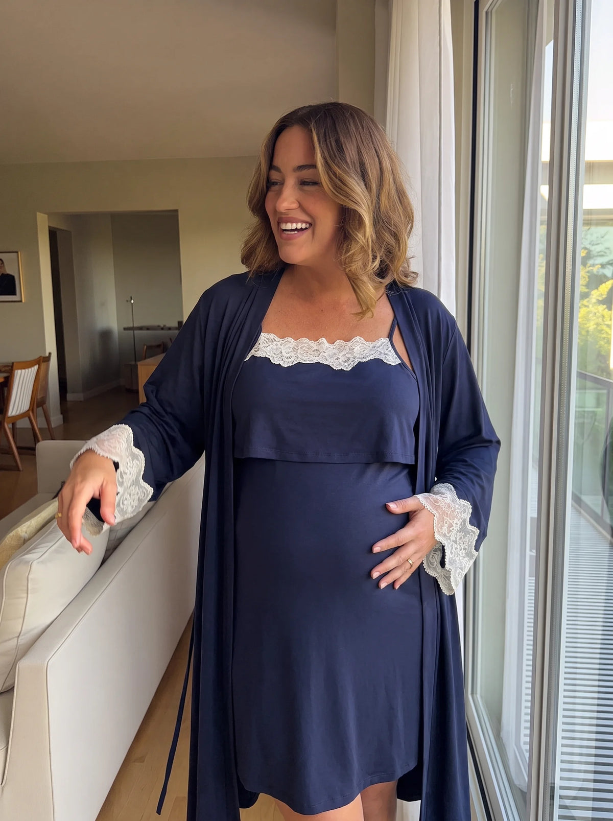 Smiling pregnant mom by the window in the navy nightgown with the robe open