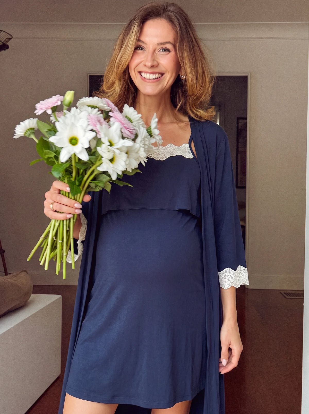 Smiling pregnant mom holding flowers in the navy nightgown and robe